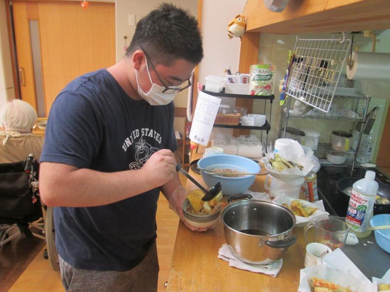 先輩が調理した蕎麦つゆを慎重に器に盛る後輩